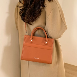 Sac fourre-tout chic en cuir orange avec poignées et bandoulière porté par un mannequin
