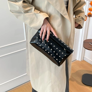 Chic black patent leather clutch with silver studs held by a model in a beige coat