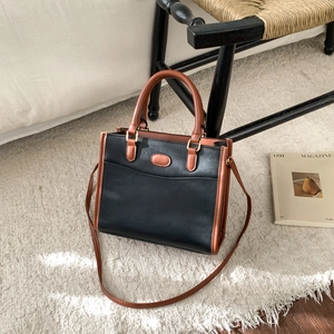 Detail of two-tone leather tote bag with gold hardware on a white carpet