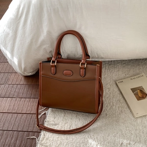Detail of brown leather tote bag with curved stitching and gold hardware on carpet