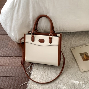Detailed close-up of beige and brown leather tote bag with gold hardware in home setting