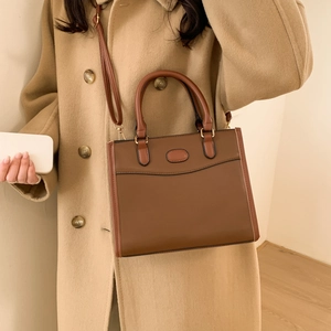 Vintage brown leather tote bag worn as a crossbody by a model in a beige cashmere coat