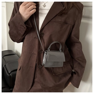 Close-up of a mini dark gray patent leather handbag worn with a brown blazer
