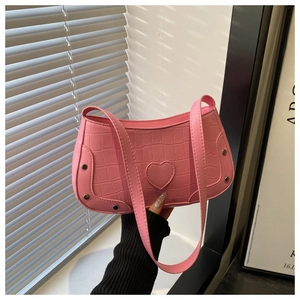 Detailed close-up of pink crocodile texture bag with heart patch and silver rivets
