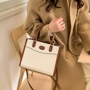 Two-tone tote bag with brown handles and beige body worn with a camel wool coat