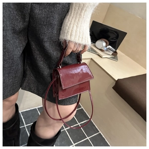 Close-up of a glossy burgundy patent leather small square bag with a handle and shoulder strap