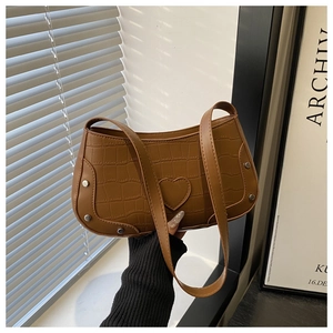 Detail of brown crocodile pattern underarm bag with heart patch and silver rivets