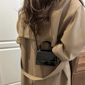 Close-up of black patent leather mini bag worn over a classic beige trench coat