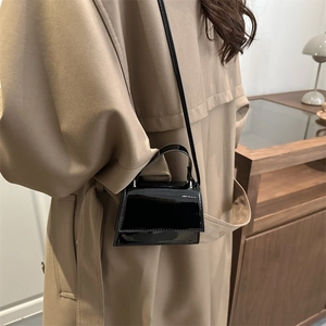 Mini glossy black leather crossbody bag styled with a khaki trench coat for a chic outfit
