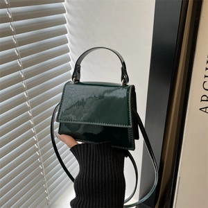 Detail view of mini dark green patent leather handbag with glossy finish and top handle