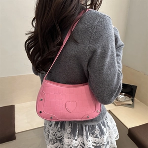 Pink croc-embossed underarm bag with heart detail and silver studs worn over shoulder