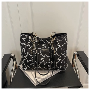 Detail of star-embroidered tote bag with gold chain strap on a black metal chair