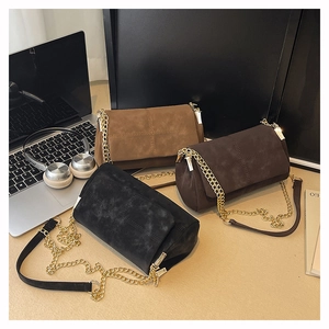 Three minimalist crossbody bags in black and brown with gold chain straps on an office desk