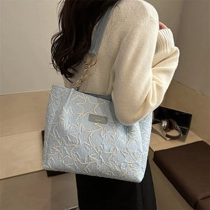 Sac cabas bleu clair avec broderie étoile et chaîne dorée porté à l'épaule