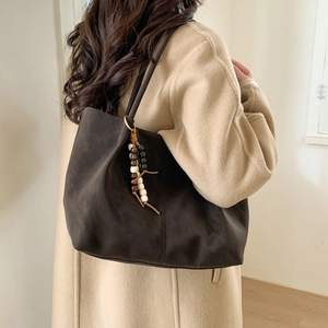 Large dark brown matte tote bag with beaded tassel charm on beige coat model