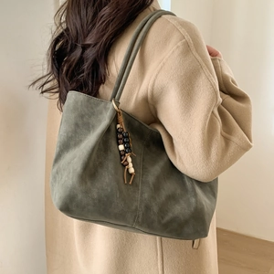Dark green suede tote bag with ethnic beaded charm shown on model in a modern style