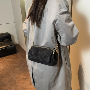 Borsa a tracolla nera opaca minimalista con catena dorata indossata su cappotto grigio