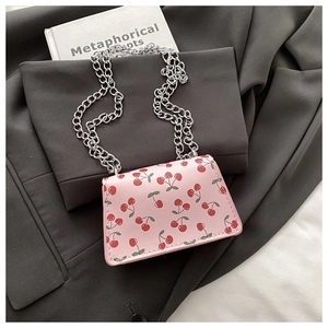 Detail of pink crossbody bag with cherry prints on gray blazer next to a book