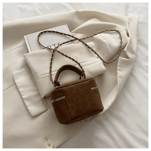 Detail of brown suede mini crossbody bag with gold chain strap on cream blazer
