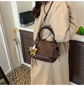 Brown frosted suede crossbody bag with teddy bear charm and striped strap shown on model