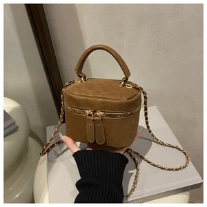 Detail of a brown leather box-style bag with chain strap and top handle held by hand