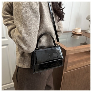 Détail du sac bandoulière en cuir verni noir avec boucles dorées et soufflets latéraux