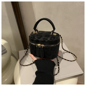Detail of a black cylinder mini bag featuring gold zippers and leopard print texture