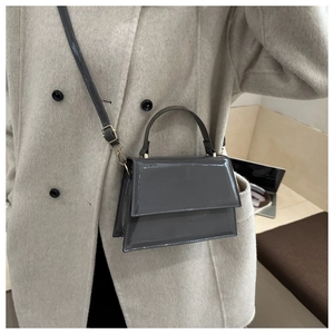 Détail d'un sac à main en cuir verni gris foncé avec finition brillante et ferrures dorées