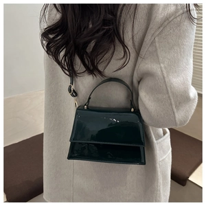 Vue détaillée d'un sac bandoulière en cuir verni vert foncé sur manteau blanc avec détails