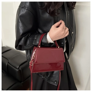 Sac à main chic en cuir verni bordeaux porté avec une veste en cuir noir élégante