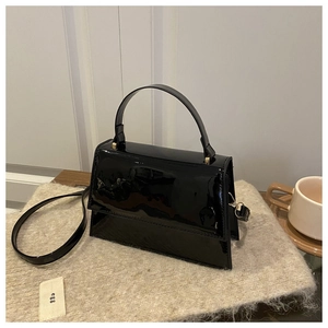 Détail d'un sac à main en cuir verni noir avec bandoulière sur fond textile chaleureux