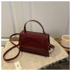 Détail du sac à main en cuir verni bordeaux avec une finition brillante et poignée