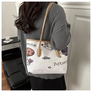 Detail of canvas tote bag featuring astronaut space illustrations and slim leather straps