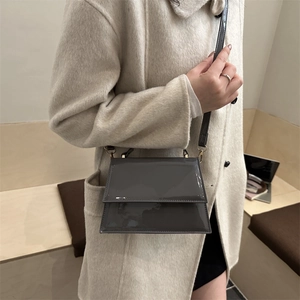 Sac bandoulière chic en cuir verni gris foncé sur un manteau en laine minimaliste