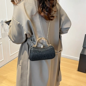 Chic black glitter evening bag with gold handle and chain strap on female model