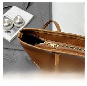Close-up of a smooth gold zipper on a brown textured leather tote bag detail view