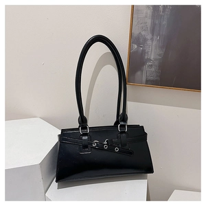 Detail of glossy black baguette bag with decorative straps on white geometric block