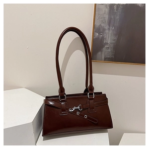 Close-up of dark brown glossy leather baguette bag with silver buckles on white pedestal