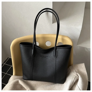 Detail of black pebbled leather tote bag with long handles on a mustard yellow chair