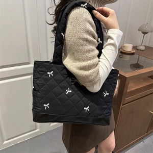 Stylish 2025 quilted tote bag with white bow embroidery on a model in a warm indoor setting
