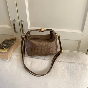 Detail view of dark brown retro handbag featuring vertical pleated texture and gold buckle