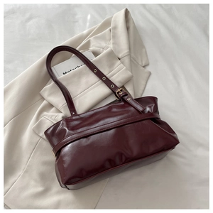 Detail view of burgundy leather shoulder bag with adjustable strap and gold metal buckles