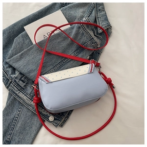 Flat lay of a light blue crossbody bag with polka dot flap and red strap detail