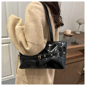 Detail of glossy black patent leather shoulder bag with golden metal buckle and eyelets