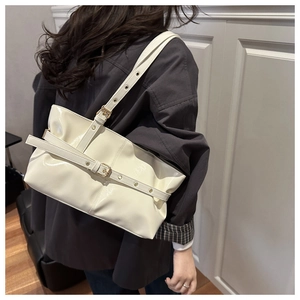 Detail of a creamy white patent leather underarm bag with metal buckle on a shoulder strap