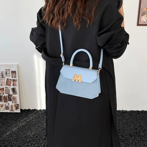 Sac à bandoulière tressé bleu clair avec détail M doré porté par un mannequin