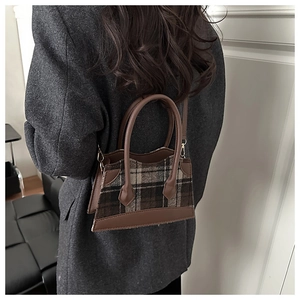 Détail de la texture en laine à carreaux et de la poignée en cuir marron d'un sac seau