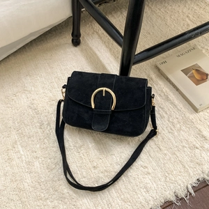 Close-up of black suede crossbody bag featuring a prominent gold round metal buckle