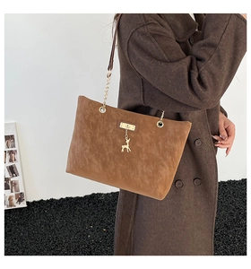 Close-up of brown suede tote bag with golden deer pendant and metal chain strap