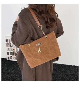 Close-up of brown suede tote bag featuring a gold deer charm and metal chain strap